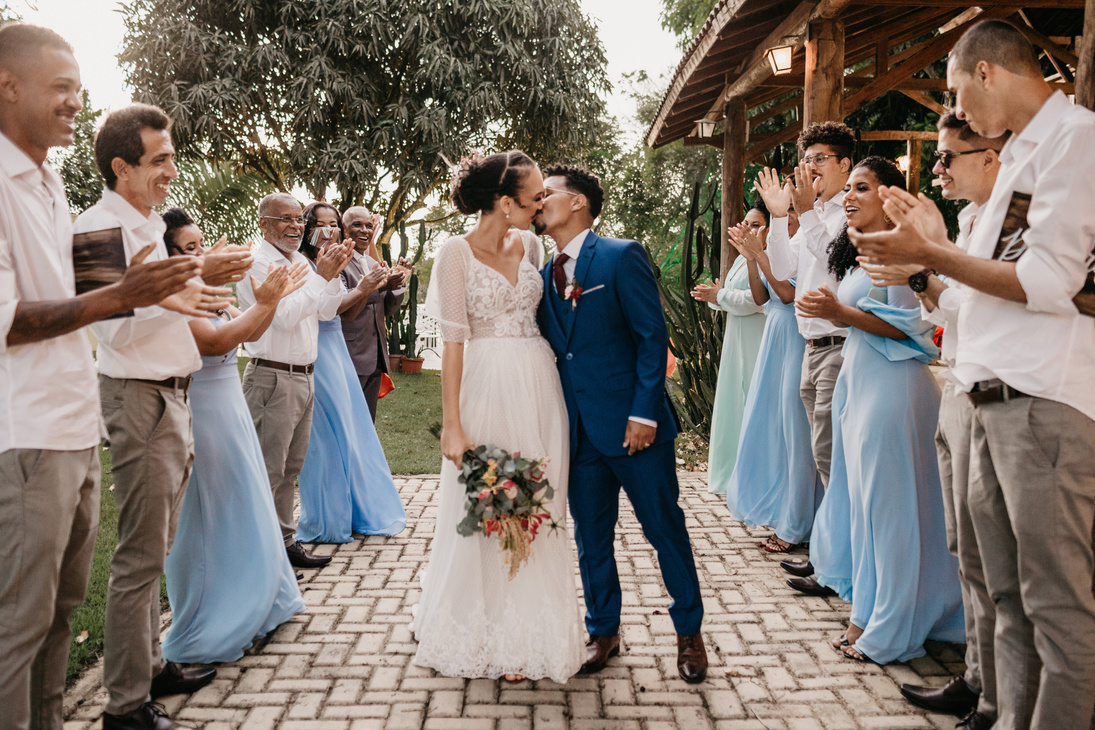 Multiethnic couple kissing between smiling guests on wedding day